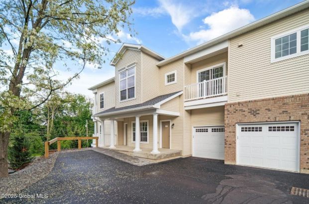 Two-story beige house with white trim, a driveway, and two garage doors.