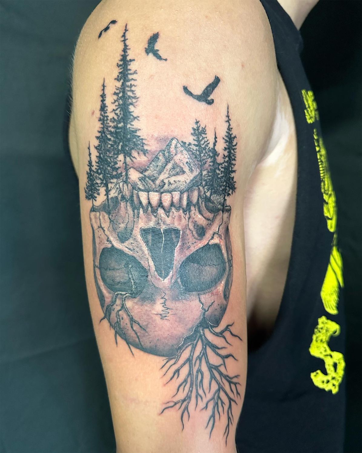 A man has a tattoo of a skull and trees on his arm