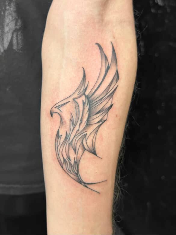 Tattoo of a stylized eagle in black ink on a person's arm, with wings spread, facing left.