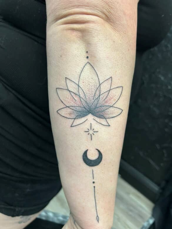Tattoo of a lotus flower, crescent moon, and star on an arm, with minimalist black line work and gray shading.