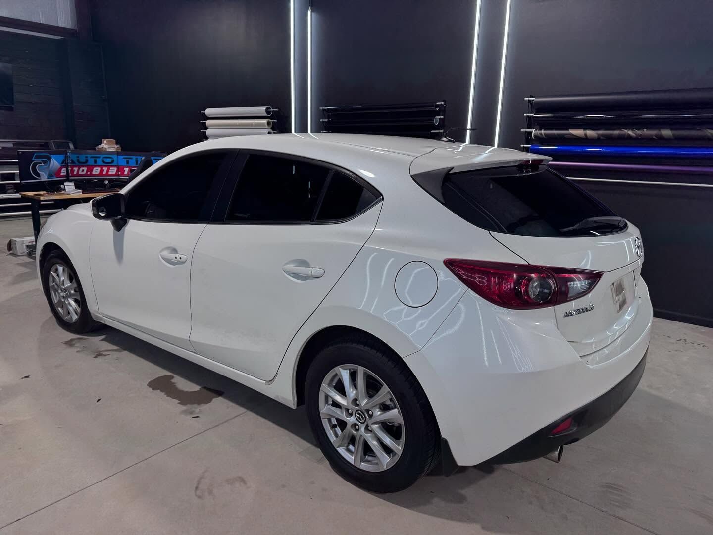 A white mazda 3 hatchback is parked in a garage.