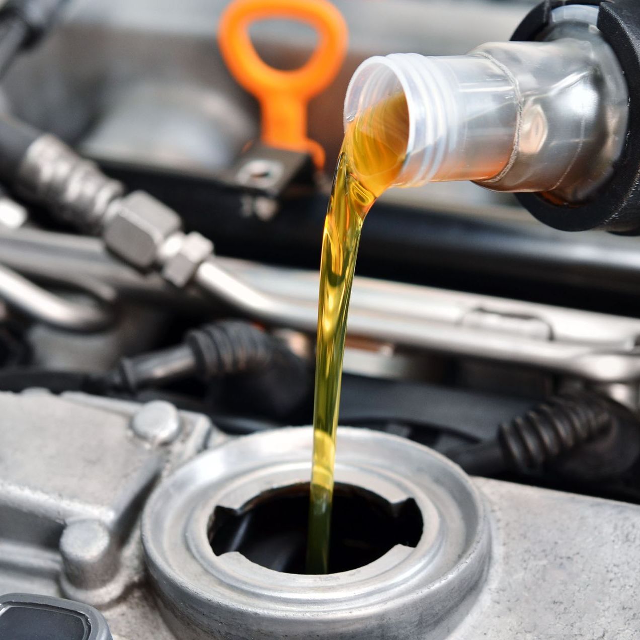 A close up of a person pouring oil into a car