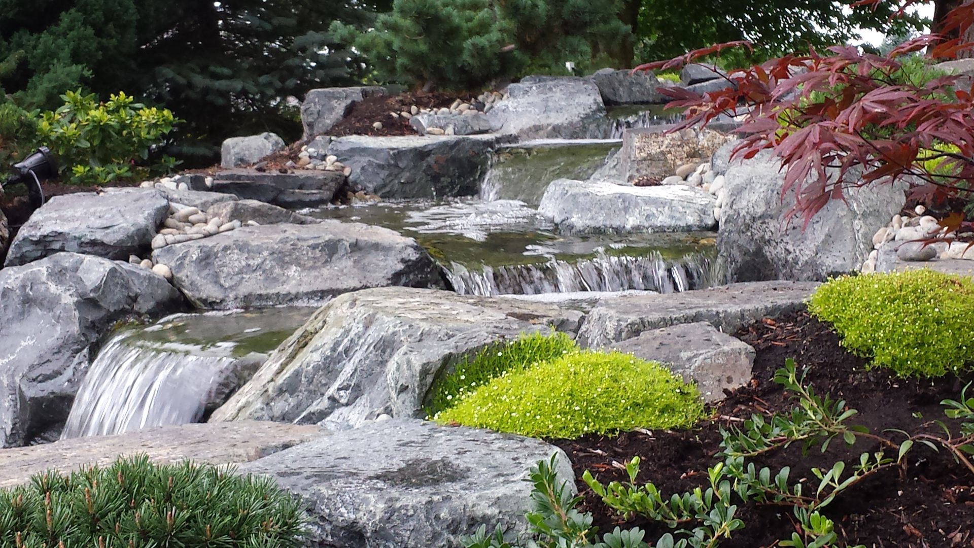 A waterfall is surrounded by rocks and trees in a garden.