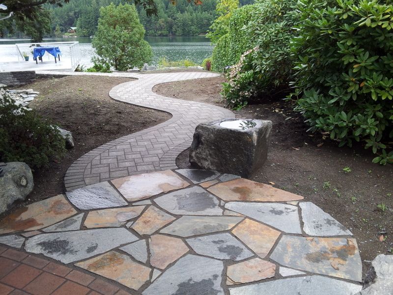 A stone walkway leading to a lake with a large rock in the middle