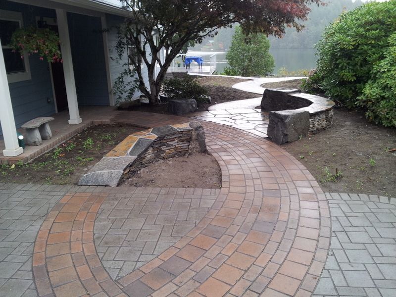 A brick walkway leading to a house with a tree in the background