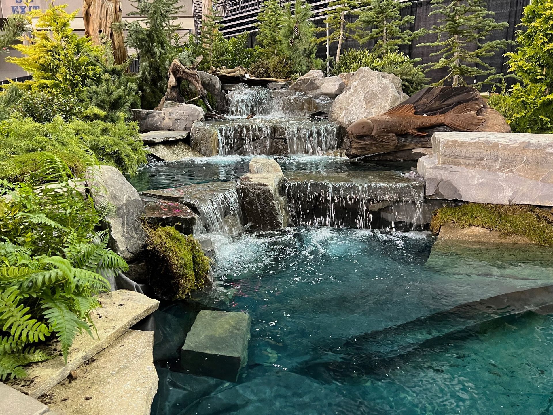 A waterfall in the middle of a swimming pool surrounded by rocks and trees.