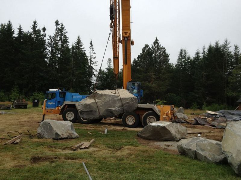 A crane is lifting a large rock in a field