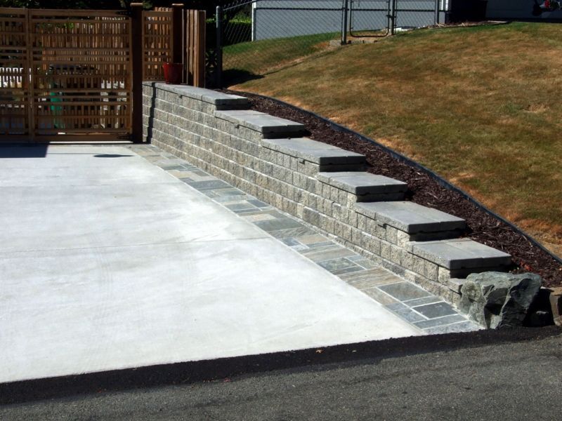 A concrete driveway with a stone wall and steps
