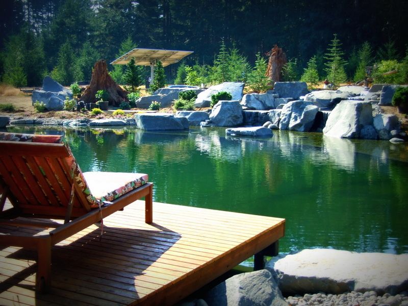 Two lounge chairs sit on a wooden deck overlooking a pond