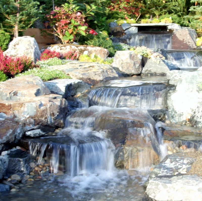 A waterfall surrounded by rocks and flowers in a garden