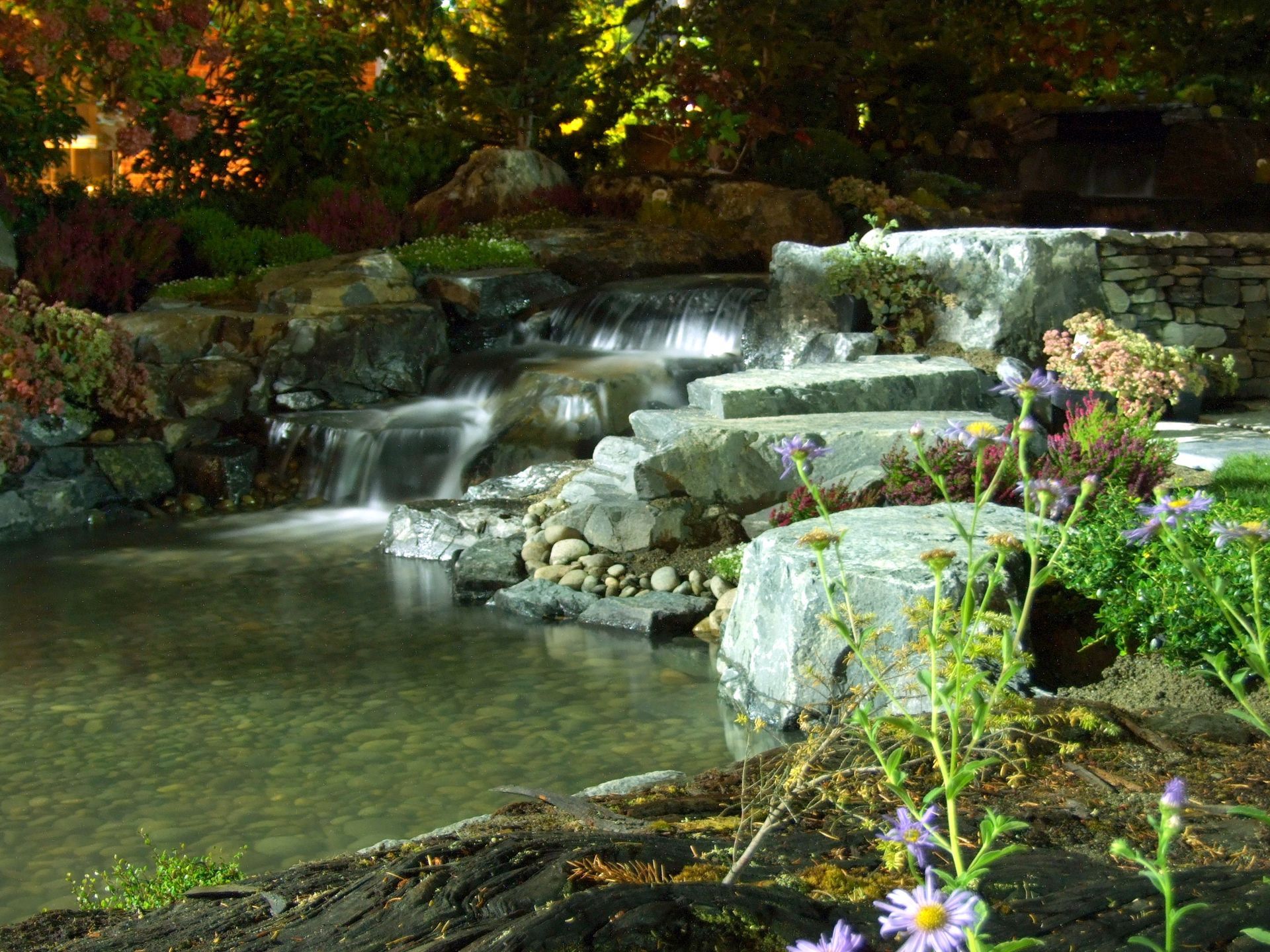 A waterfall is surrounded by rocks and flowers in a garden