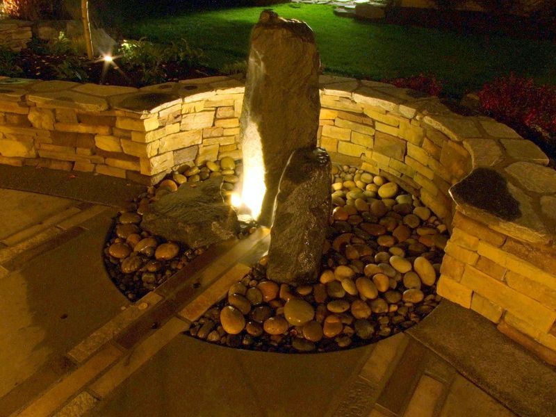 A water fountain is lit up at night and surrounded by rocks.