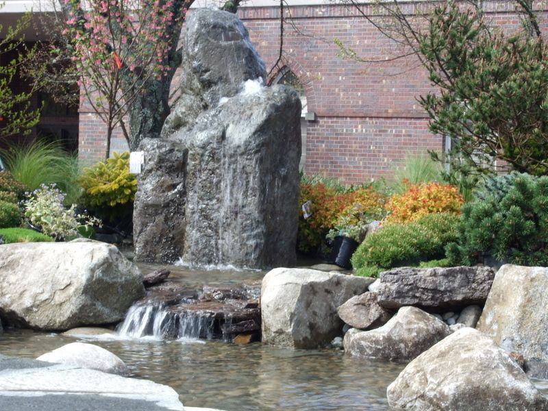A waterfall surrounded by rocks and trees in front of a brick building
