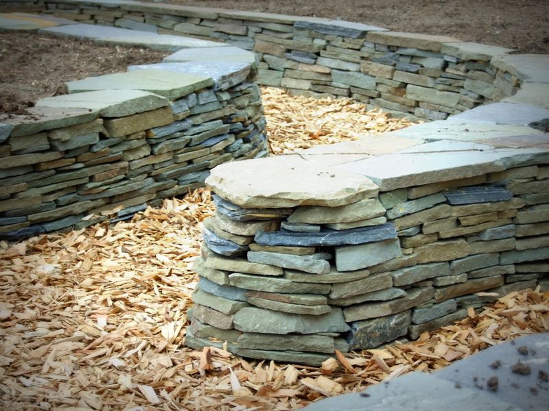 A stone wall is surrounded by wood chips and leaves
