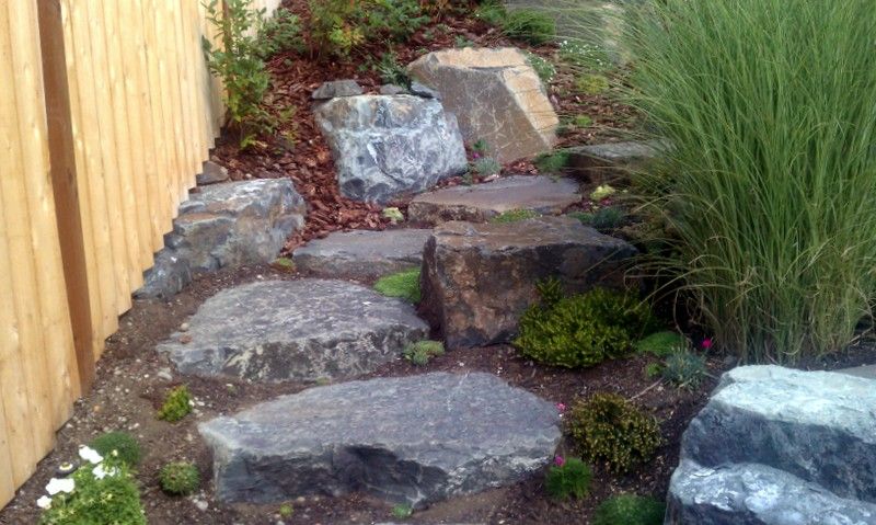 A wooden fence is surrounded by rocks and plants in a garden.