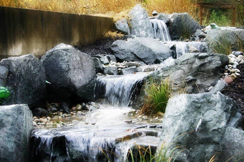 A small waterfall is surrounded by rocks and grass