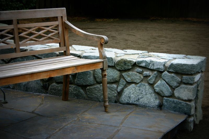 A wooden bench sits next to a stone wall