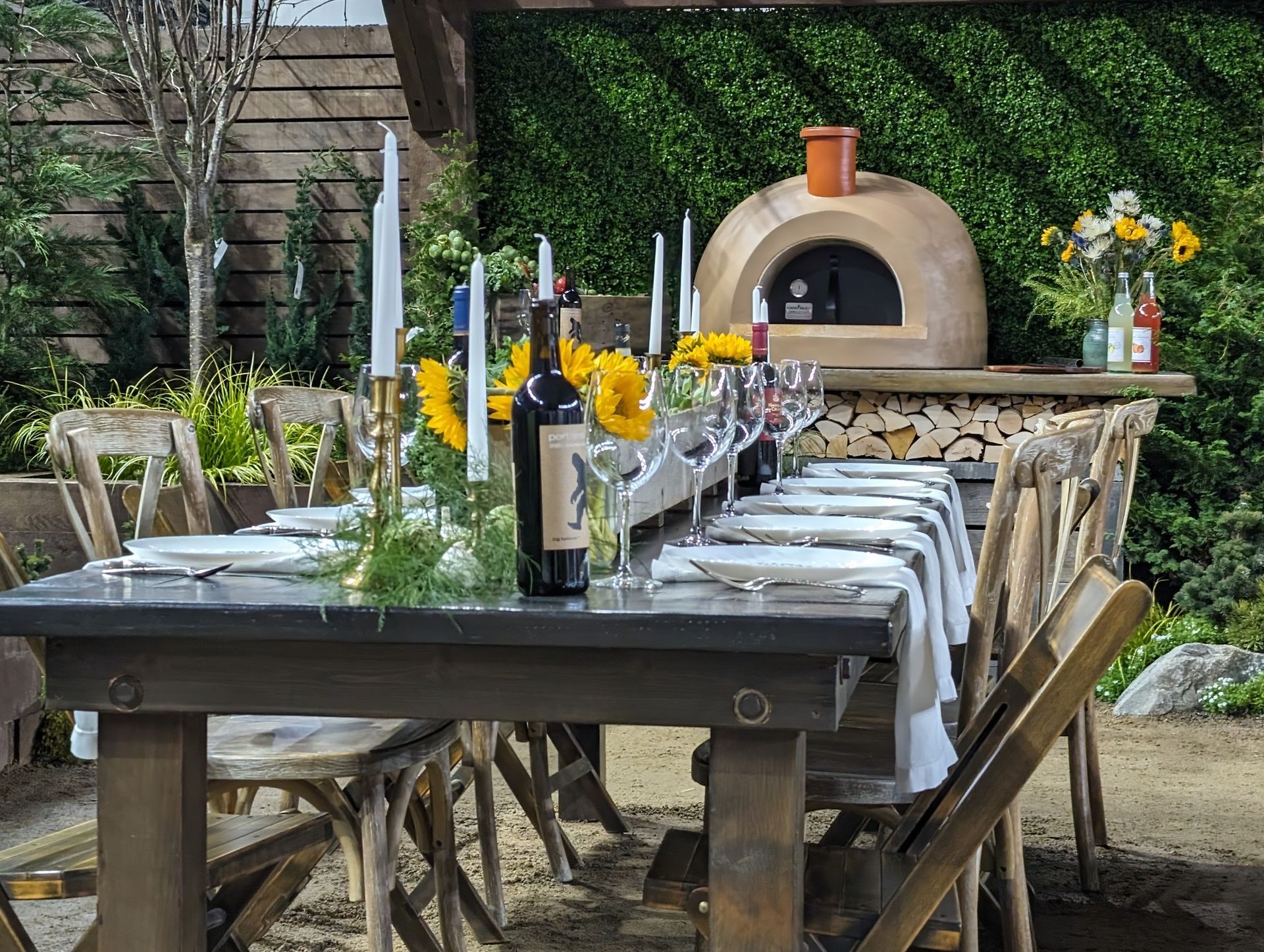 A long table with wine bottles , candles , and sunflowers on it.