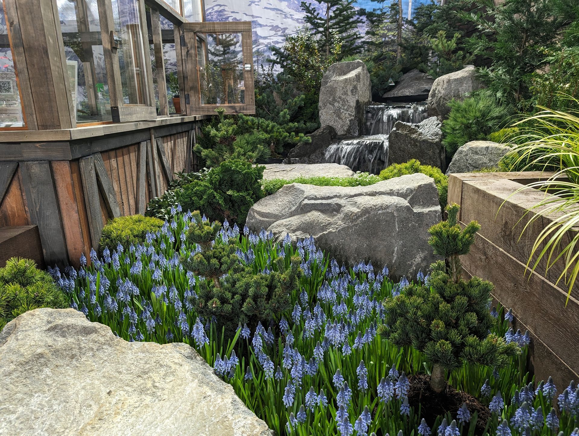 A garden with flowers , rocks , trees and a waterfall.