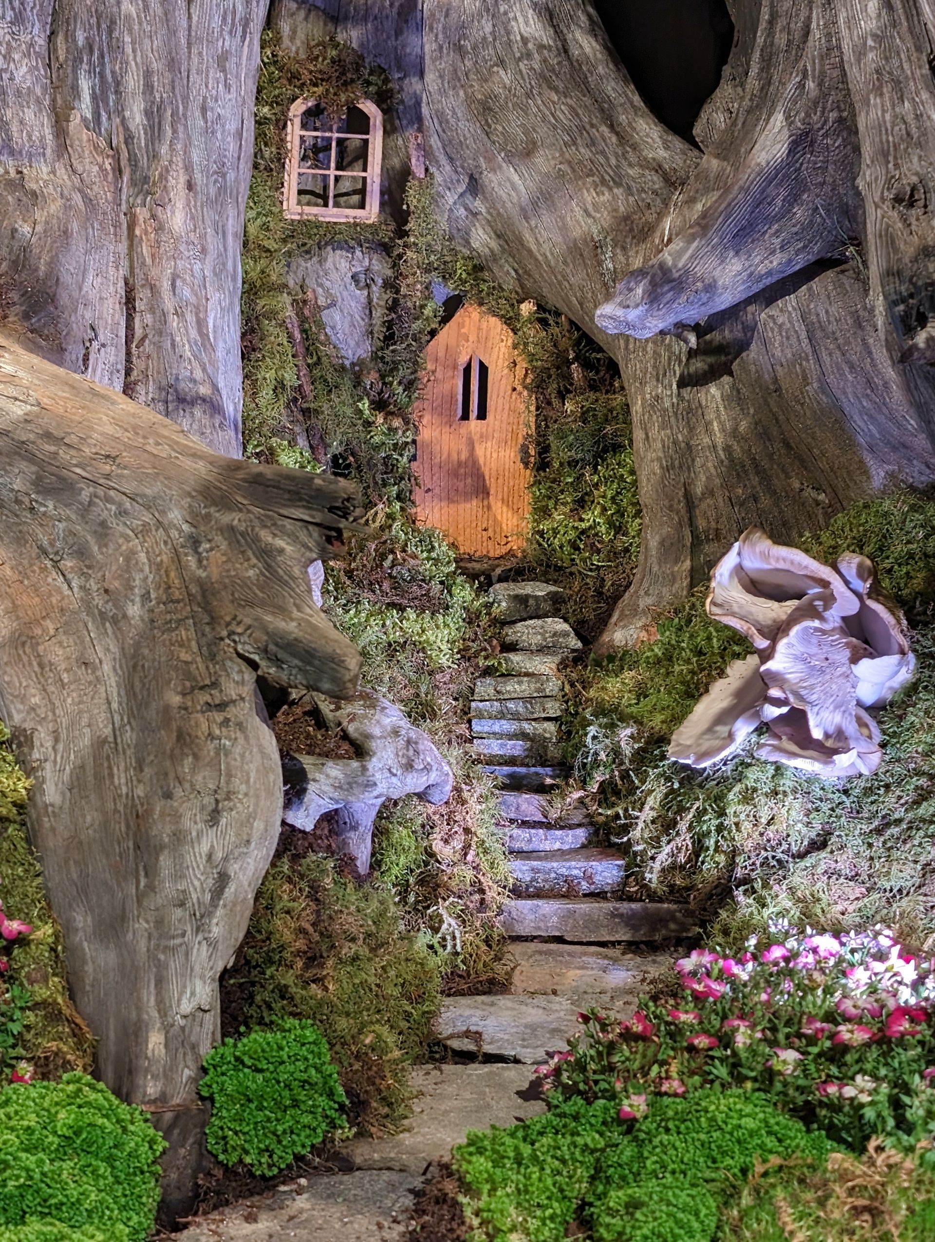 A fairy house in the middle of a forest with stairs leading to it.