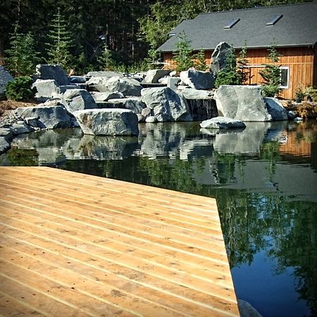 A wooden deck overlooking a pond with a house in the background