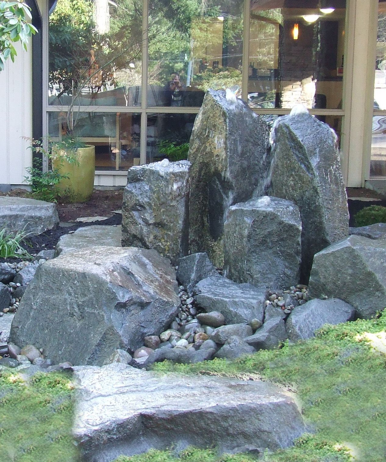 A large rock in the middle of a garden with a house in the background