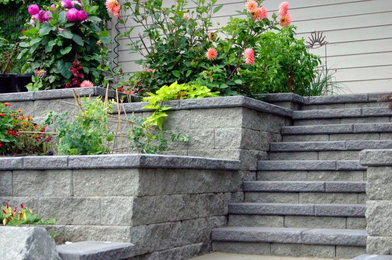 a set of stairs leading up to a stone wall with flowers