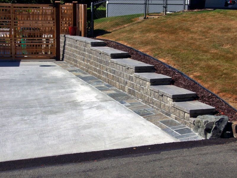 a concrete driveway with a stone wall and steps
