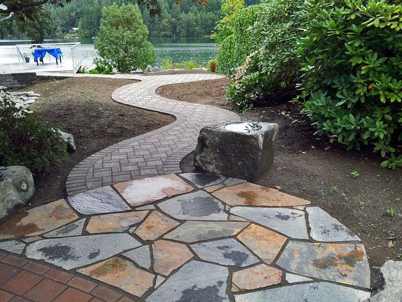 a stone walkway leading to a lake with a large rock in the middle
