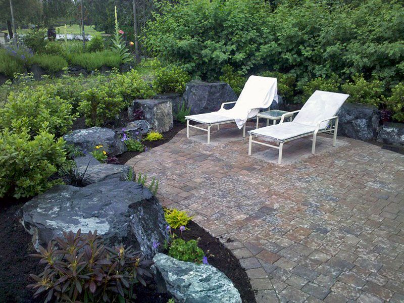 two white lounge chairs are sitting on a patio surrounded by rocks