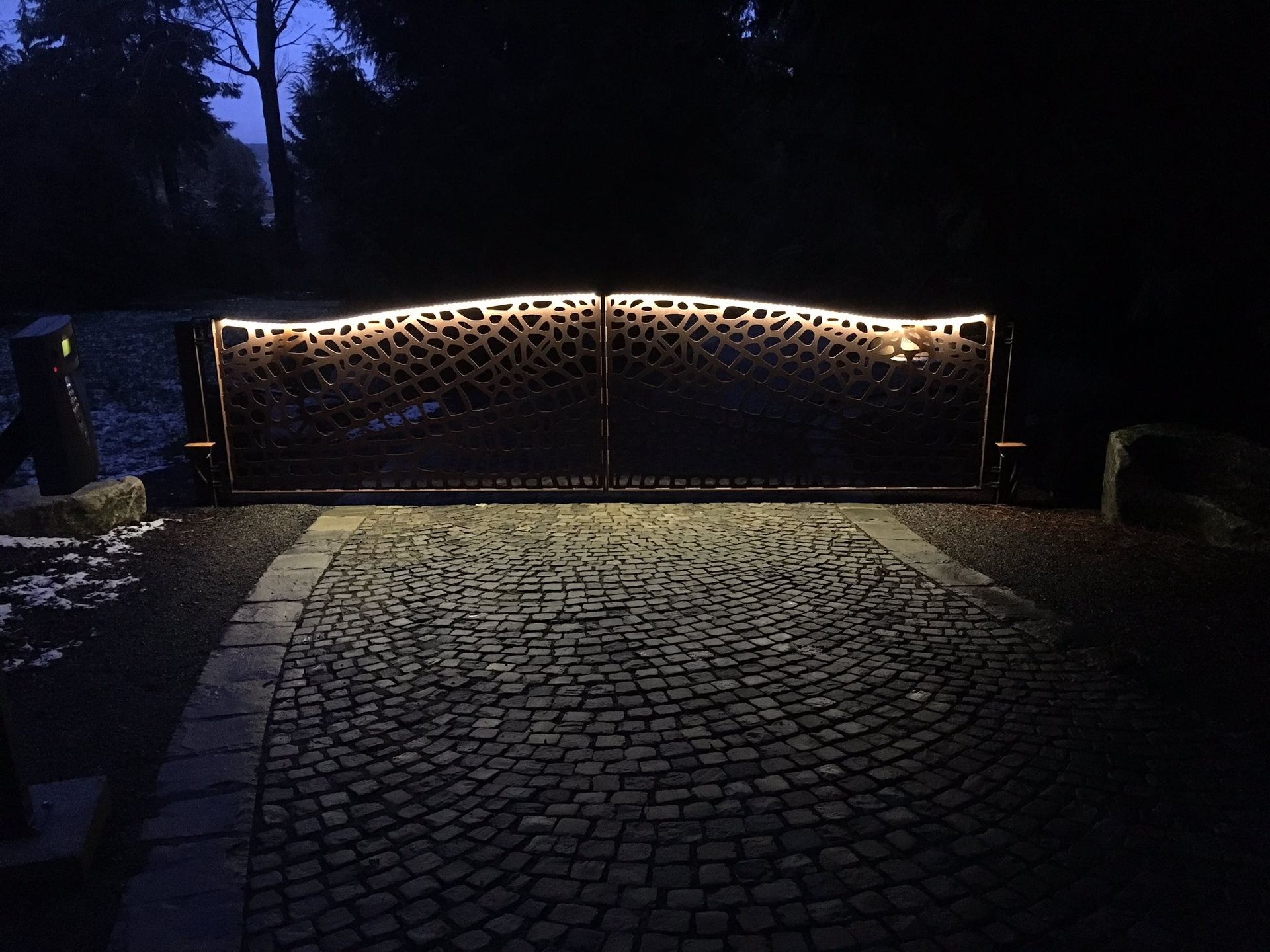 a gate is lit up at night on a cobblestone driveway