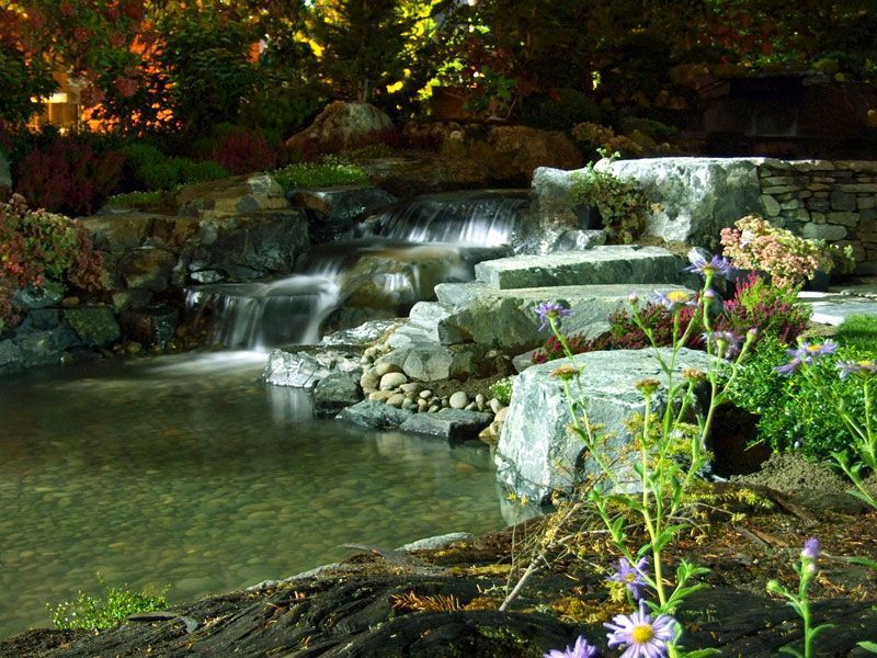 a waterfall is surrounded by rocks and flowers in a garden