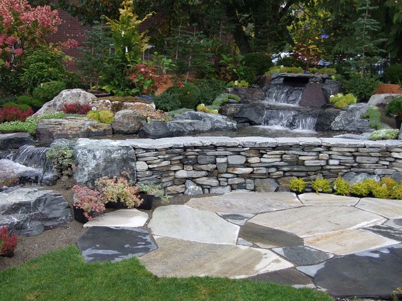 a garden with a waterfall and a stone wall