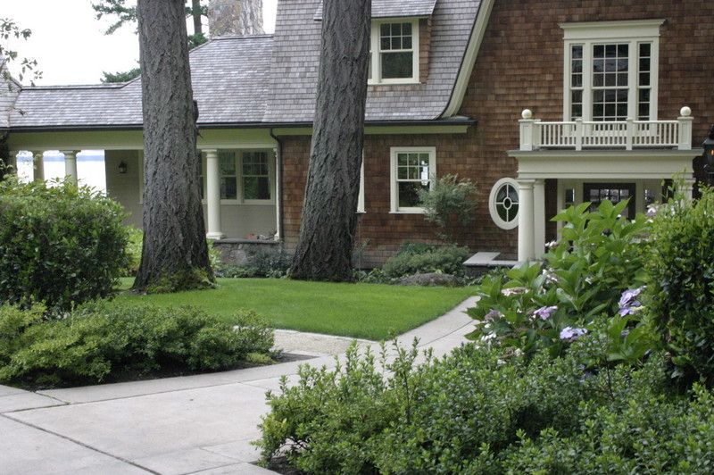 a large brick house with a porch surrounded by trees and bushes