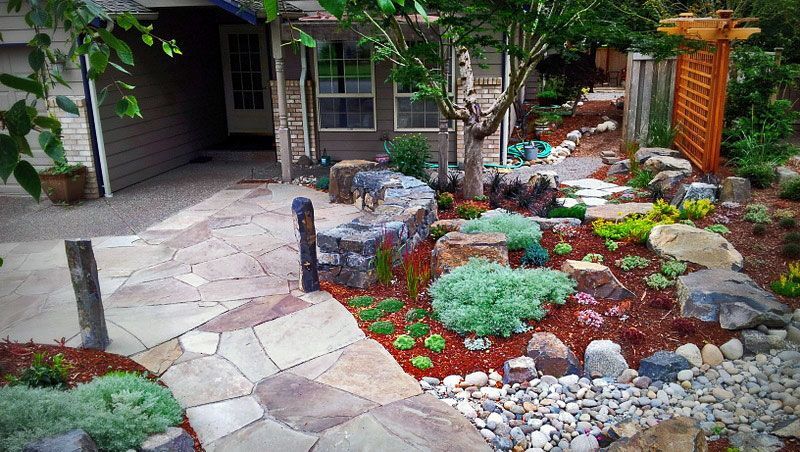 a stone walkway leading to a house surrounded by rocks and plants