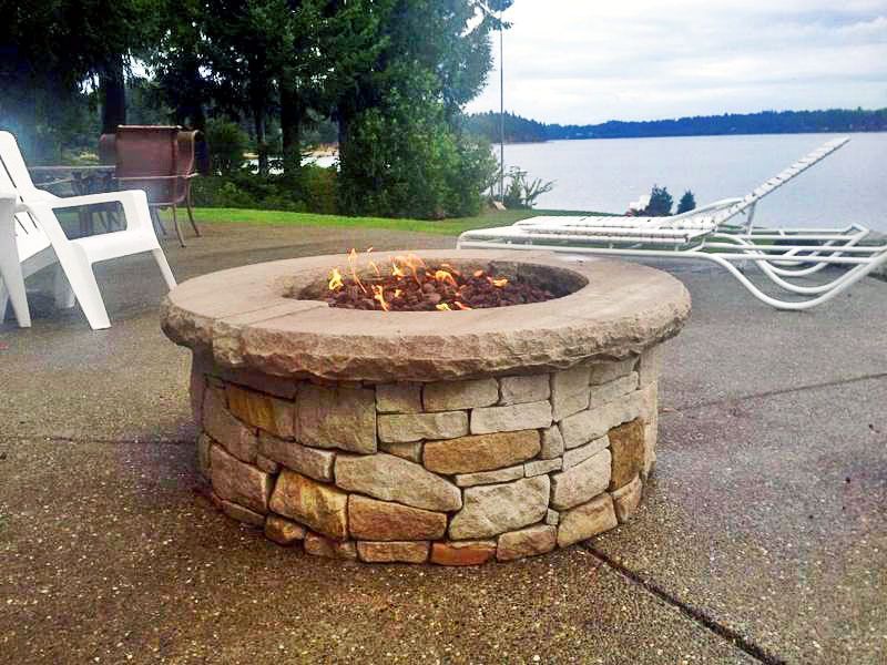 a fire pit is sitting on a patio next to a lake