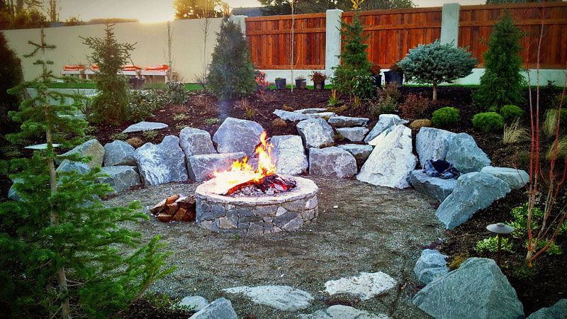 a fire pit surrounded by rocks and trees in a garden