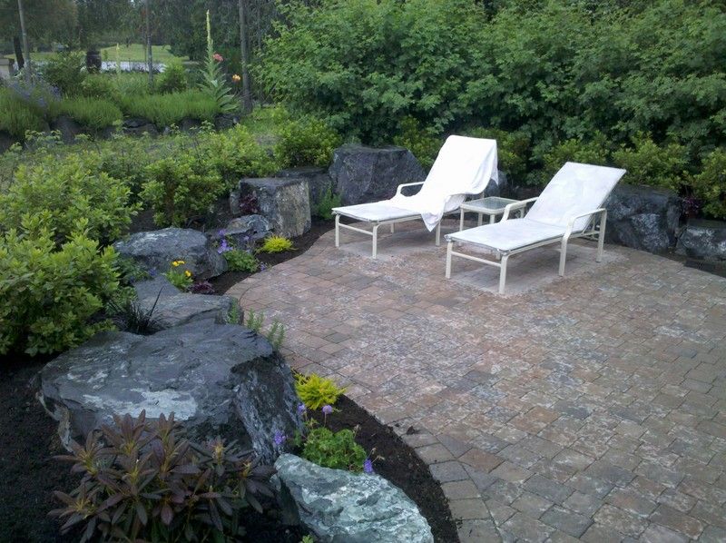 two white lounge chairs are sitting on a patio in a garden