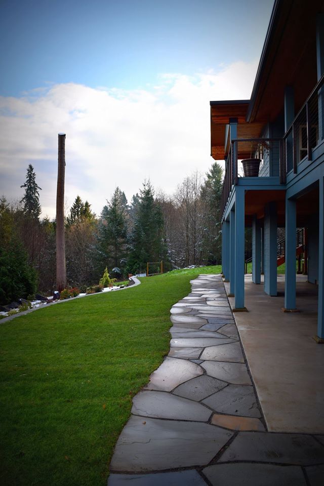 a stone walkway leading to a house with a lush green lawn