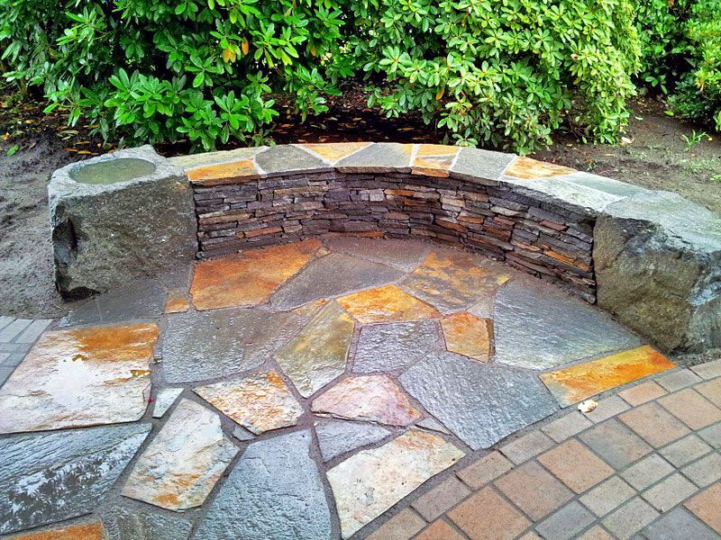 a stone bench is sitting on a brick patio next to a stone wall