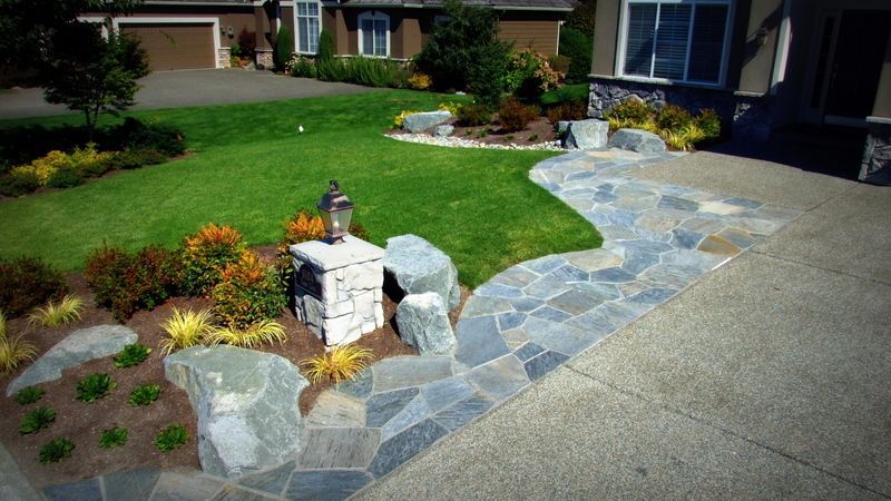 a stone walkway leading to a house with a lush green lawn