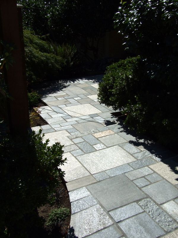 a stone walkway surrounded by trees and bushes on a sunny day