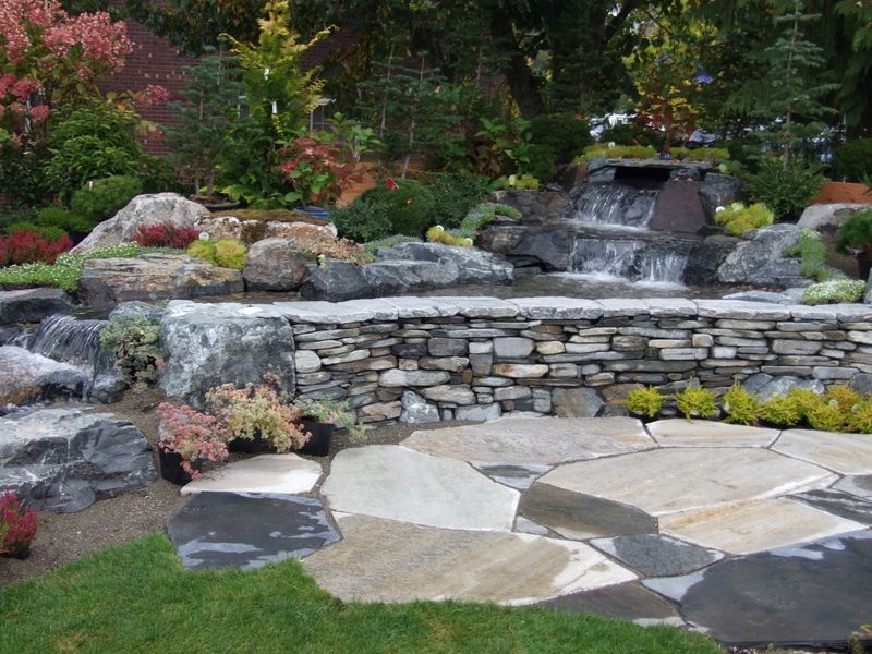 a garden with a waterfall and a stone wall