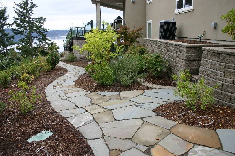 a stone walkway leading to a house with a view of the water