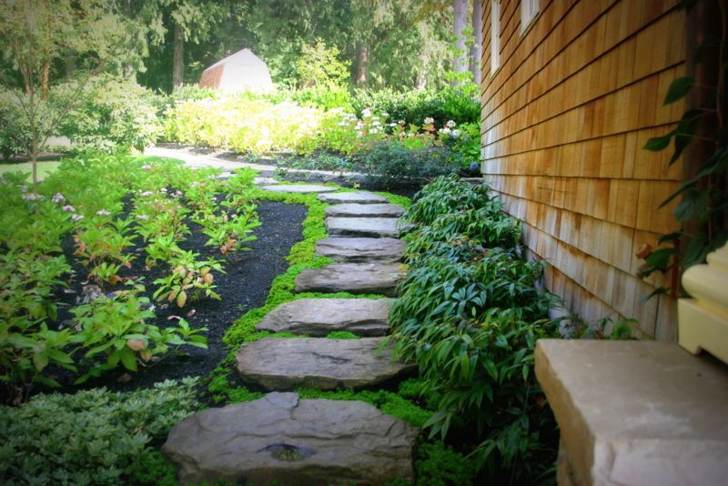 a stone walkway leading to a house in a garden