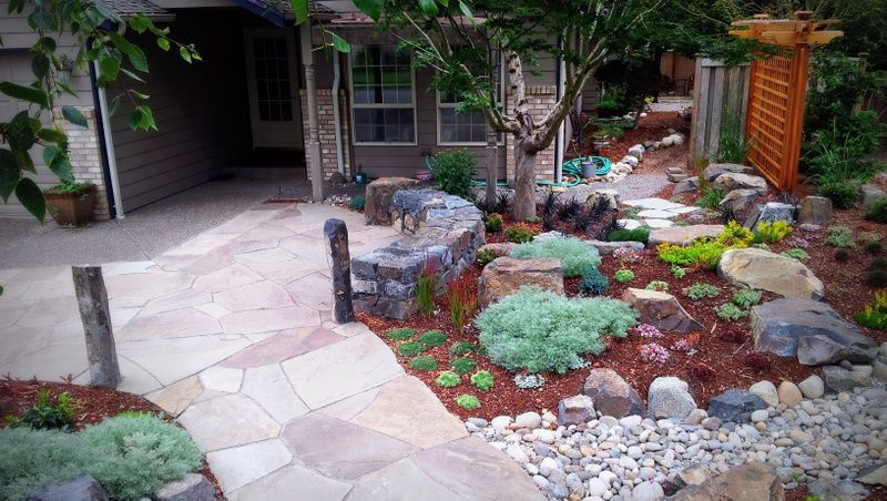 a stone walkway leading to a house surrounded by rocks and plants