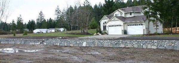 a white house with two garages is sitting in the middle of a muddy field
