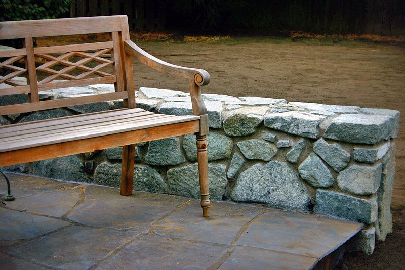 a wooden bench sits next to a stone wall