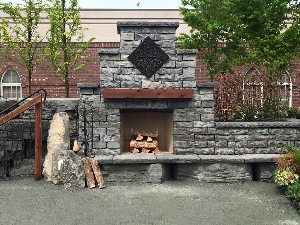 A stone fireplace with logs in it in front of a brick building.