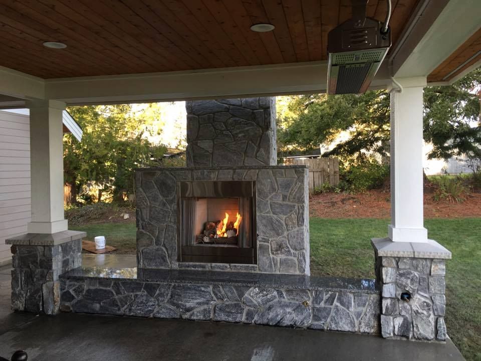 A stone fireplace is sitting under a covered porch.